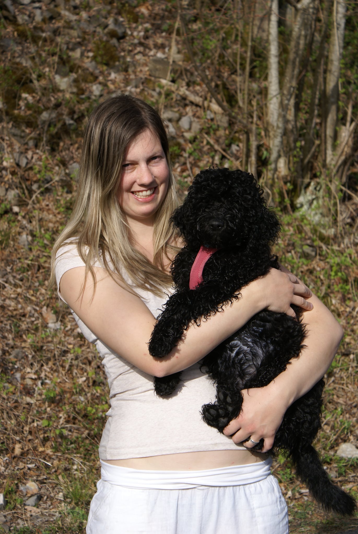 Selina und Malou: Lächelnde Frau hält einen schwarzen Hund mit lockigem Fell im Arm